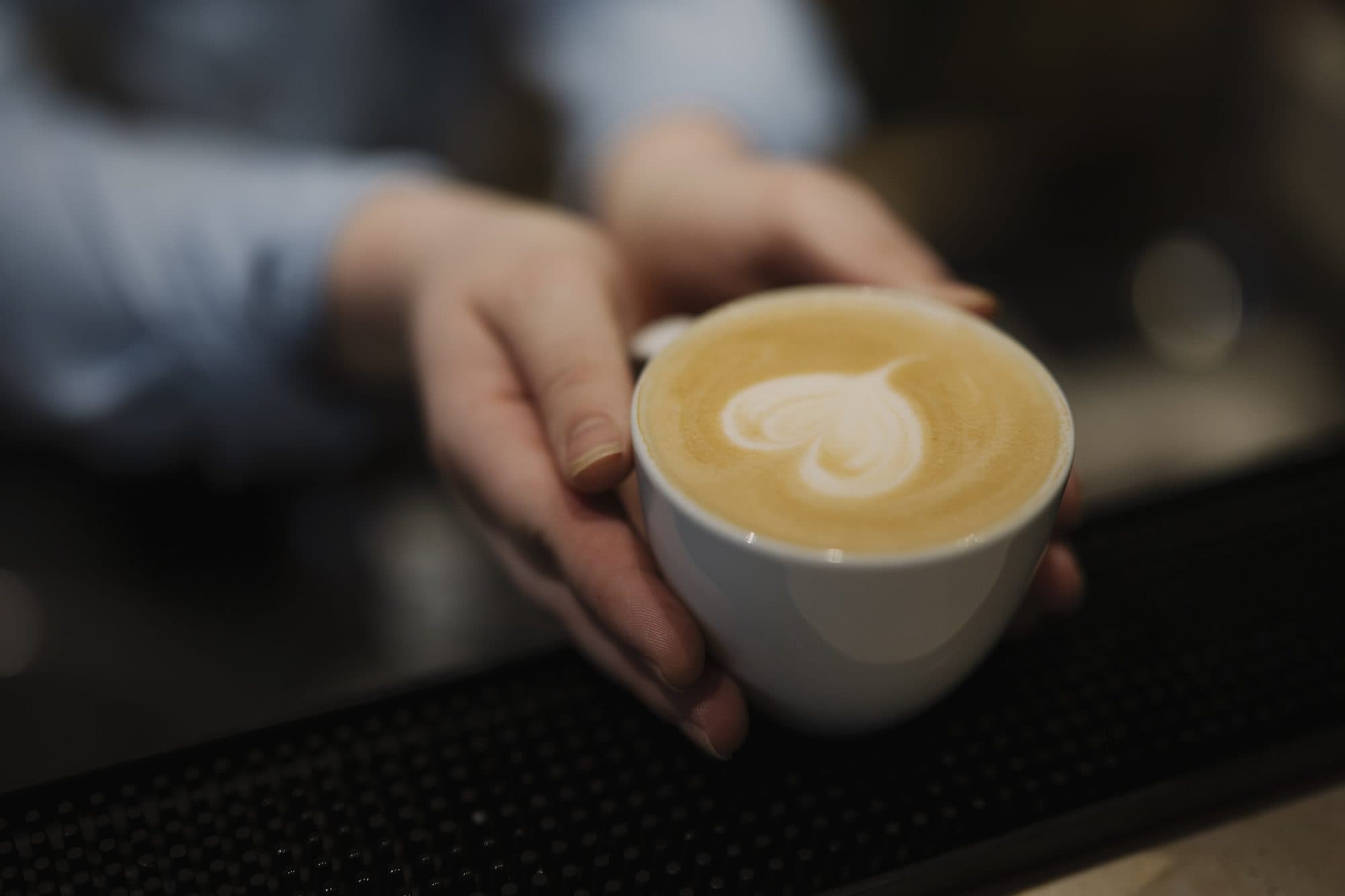 Taza de café con arte latte en forma de corazón, servida en la barra.